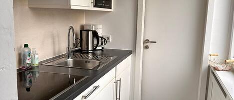 A compact kitchen with a black countertop, stainless steel appliances, and white cabinetry.