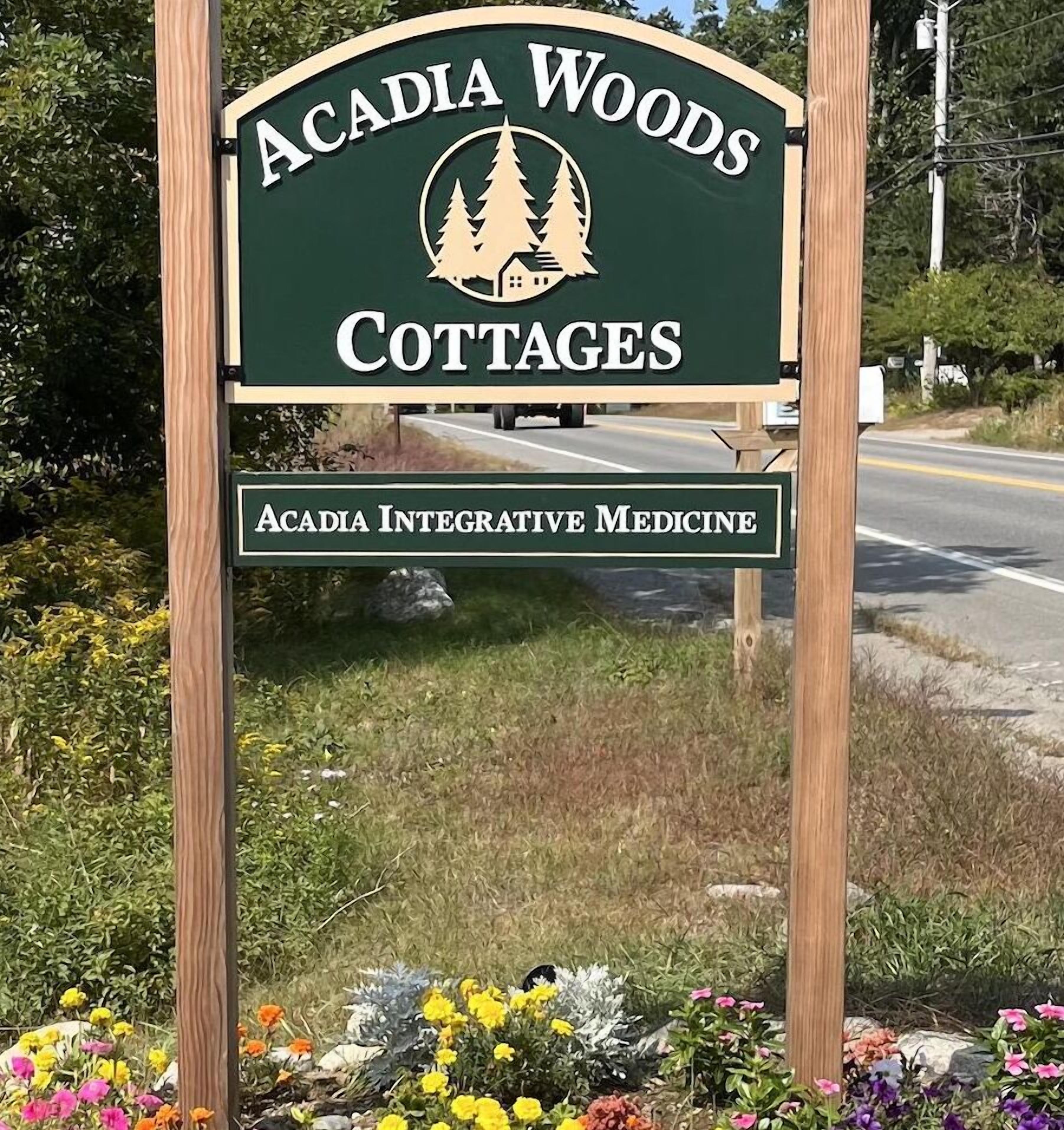 Een bordje voor Acadia Woods Cottages met een logo van bomen en een huis, en de vermelding van Acadia Integrative Medicine.
