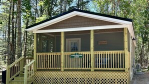 Un piccolo chalet in legno con veranda, con la scritta "Popplestone Point", immerso tra gli alberi.