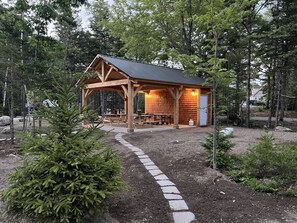 A wooden cabin with a metal roof, surrounded by trees and a gravel path.
