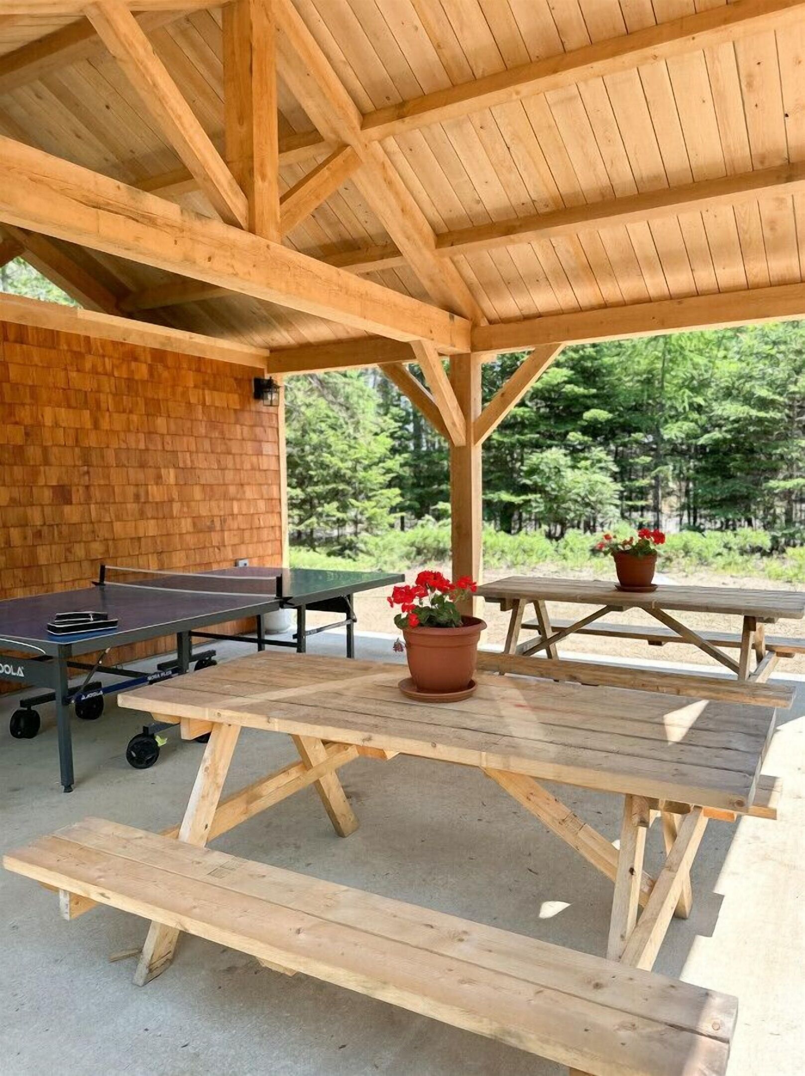 Et overdækket udendørs område med picnicborde, et bordtennisbord og en murstensvæg.