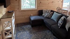 Interior acogedor de una cabaña con un sofá de color oscuro, una mesita de madera y un televisor colgado en la pared.