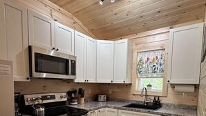 A modern kitchen with white cabinets, stainless steel appliances, a granite countertop, and a wooden ceiling. - Marshall Lodge. At the heart of Acadia and MDI! (Mount Desert)