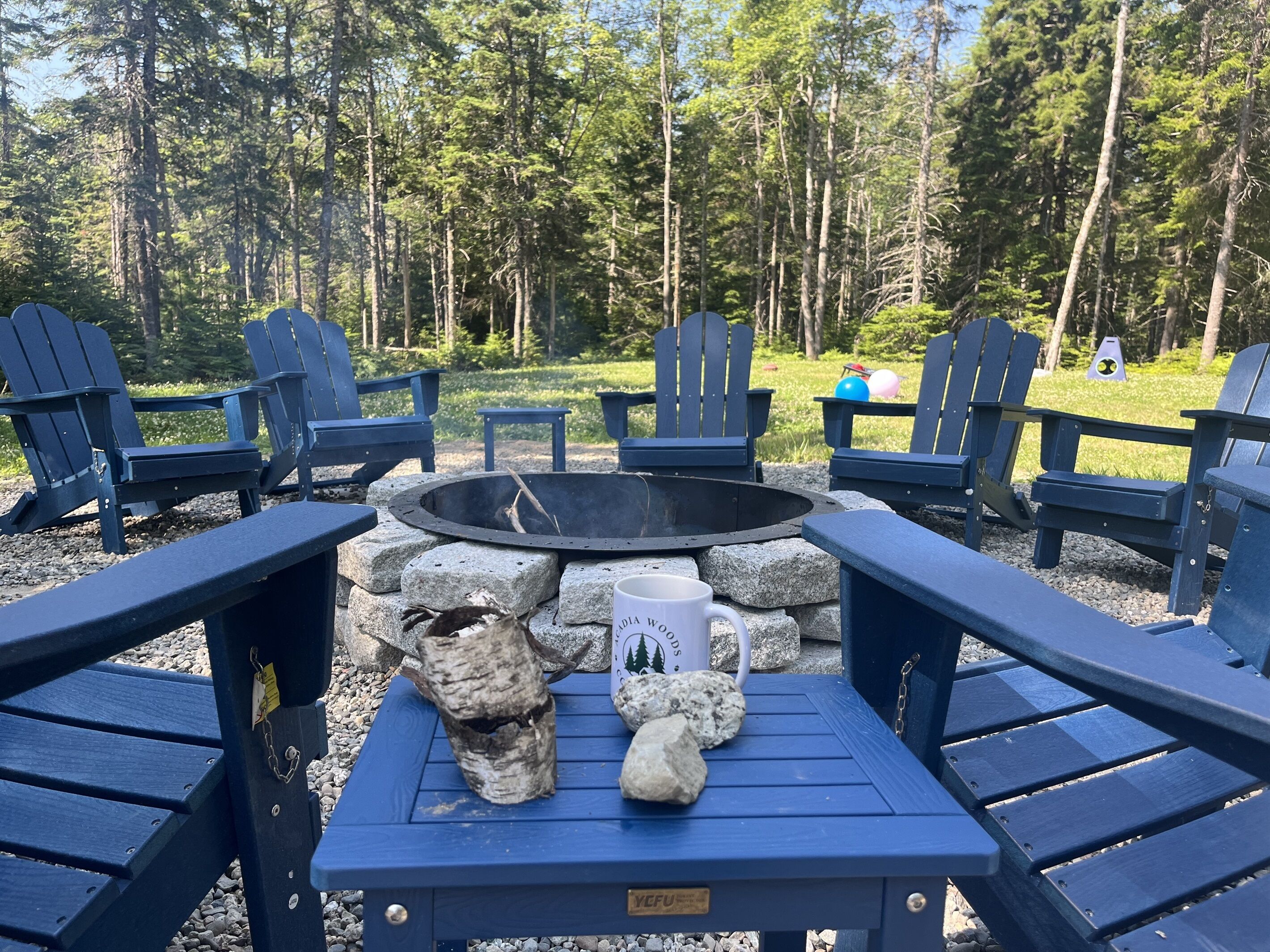 Eine Sitzgruppe mit Adirondack-Stühlen und einem Steinkamin, umgeben von einem Wald.