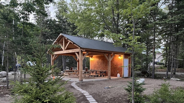Une cabane en bois avec un toit en métal, entourée d’arbres et bordée d’un chemin de gravier.