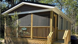 Une cabane en bois avec un porche couvert, une enseigne indiquant « Havre de paix enchanté » et une allée gravillonnée.