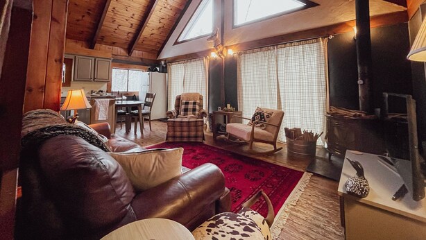 A cozy cabin interior with a high ceiling, wooden beams, a fireplace, a dining area, and a living room with leather furniture. - Cozy chalet near lakes and mountains. Pet friendly! (Lovell)