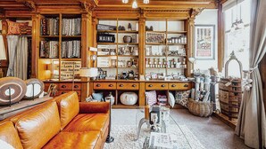 A cozy, well-organized room with a vintage aesthetic, featuring a leather sofa, wooden shelves filled with various items, and a large window providing natural light. - Cozy chalet near lakes and mountains. Pet friendly! (Lovell)