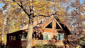 A wooden cabin with a sloped roof, a chimney, and a deck with stairs leading to the entrance. - Cozy chalet near lakes and mountains. Pet friendly! (Lovell)
