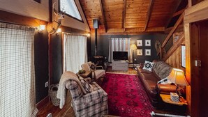 A cozy cabin interior with a wooden ceiling, a fireplace, a television, and a red rug. - Cozy chalet near lakes and mountains. Pet friendly! (Lovell)