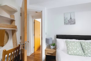A bedroom with a bed, bedside table, lamp, and a painting of a cityscape. - Skyvillion - Central Ldn 3bed Flat Ladbroke Grove (London)