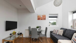 A modern living room with a flat-screen TV, a dining table with chairs, a sofa, and a ceiling light fixture. - Skyvillion - Central Ldn 3bed Flat Ladbroke Grove (London)