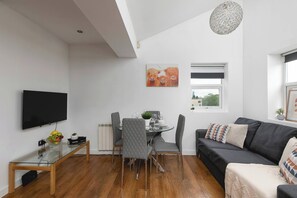 Una sala de estar moderna con una televisión de pantalla plana, una mesa de comedor con sillas, un sofá y una lámpara en el techo.