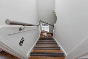 Una escalera con barandilla de metal, peldaños de madera y un pequeño ventanal en la parte superior.
