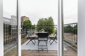 Een balkon met een tafel, stoelen, een bloempot en uitzicht op gebouwen en bomen.