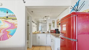 Une cuisine avec des meubles blancs, un réfrigérateur rouge et une fresque colorée sur le mur.
