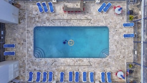 Vue aérienne d’une piscine rectangulaire, avec des chaises longues et une table sur une terrasse carrelée.