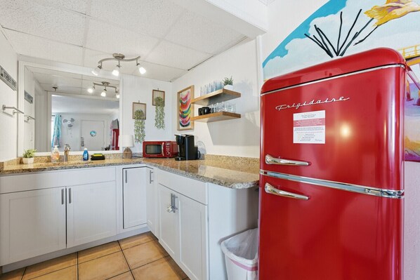 Una cocina con armarios blancos, un refrigerador rojo, un microondas y una cafetera.