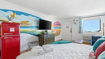 Ein Schlafzimmer mit Meeresblick, einer Strandmalerei, einem roten Kühlschrank und einem Bett mit weißer Bettdecke.