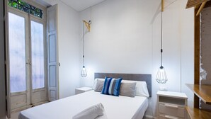 A neatly made bed with a folded towel, a bedside table, and a nightstand. There is a window with a view of greenery outside. - The Vella Apartment by Florit Flats (Valencia)