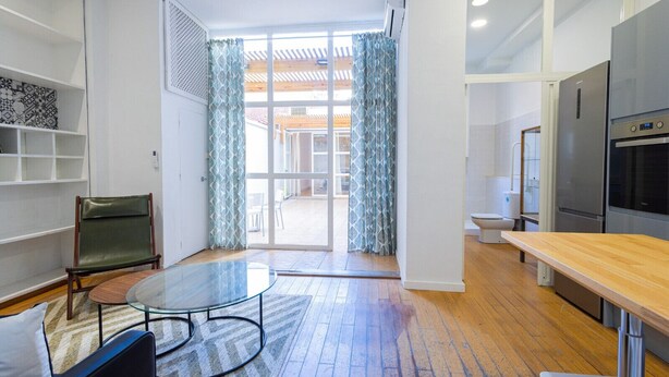 A modern kitchen with a built-in oven and refrigerator, a dining area with a glass table, and a view through a glass door to an outdoor patio. - The Vella Apartment by Florit Flats (Valencia)