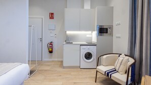 A compact hotel room with a bed, a washing machine, a microwave, and a sofa.
