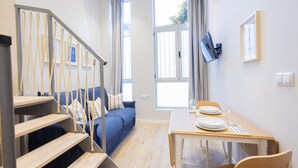 Un salon moderne avec un escalier, un canapé, une table à manger pour deux personnes et un téléviseur fixé au mur.