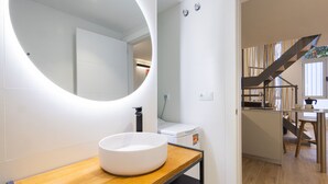 Une salle de bain moderne avec un miroir rond, un lavabo blanc et un plan de travail en bois.