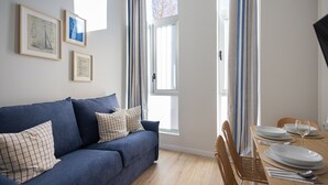 A room with a blue sofa, a dining table set with plates and a glass, and framed artwork on the wall.