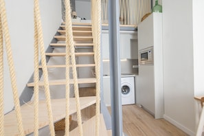 Un escalier avec une barrière en corde, un lave-linge et un four à micro-ondes dans un espace cuisine moderne.