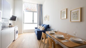 Una cocina moderna con lavadora, un comedor con una mesa de madera preparada para dos personas y un sofá azul.