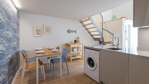 A compact kitchen with a washing machine, a dining area with a table and chairs, and a staircase with a striped railing.