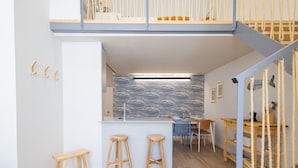 A modern kitchen with a white island, wooden stools, and a dining area with a blue chair.