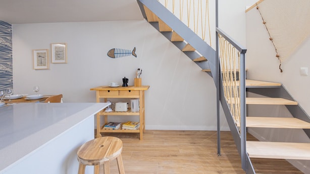 A modern kitchen with a wooden island, a wooden dining table, and a staircase with a metal railing.