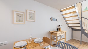 A dining area with a wooden table set for four, two framed nautical charts on the wall, and a staircase with a wooden railing.