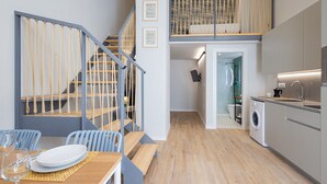 Eine moderne Küche mit Waschmaschine, ein Essbereich mit Tisch für zwei Personen und eine Treppe mit Seilgeländer.