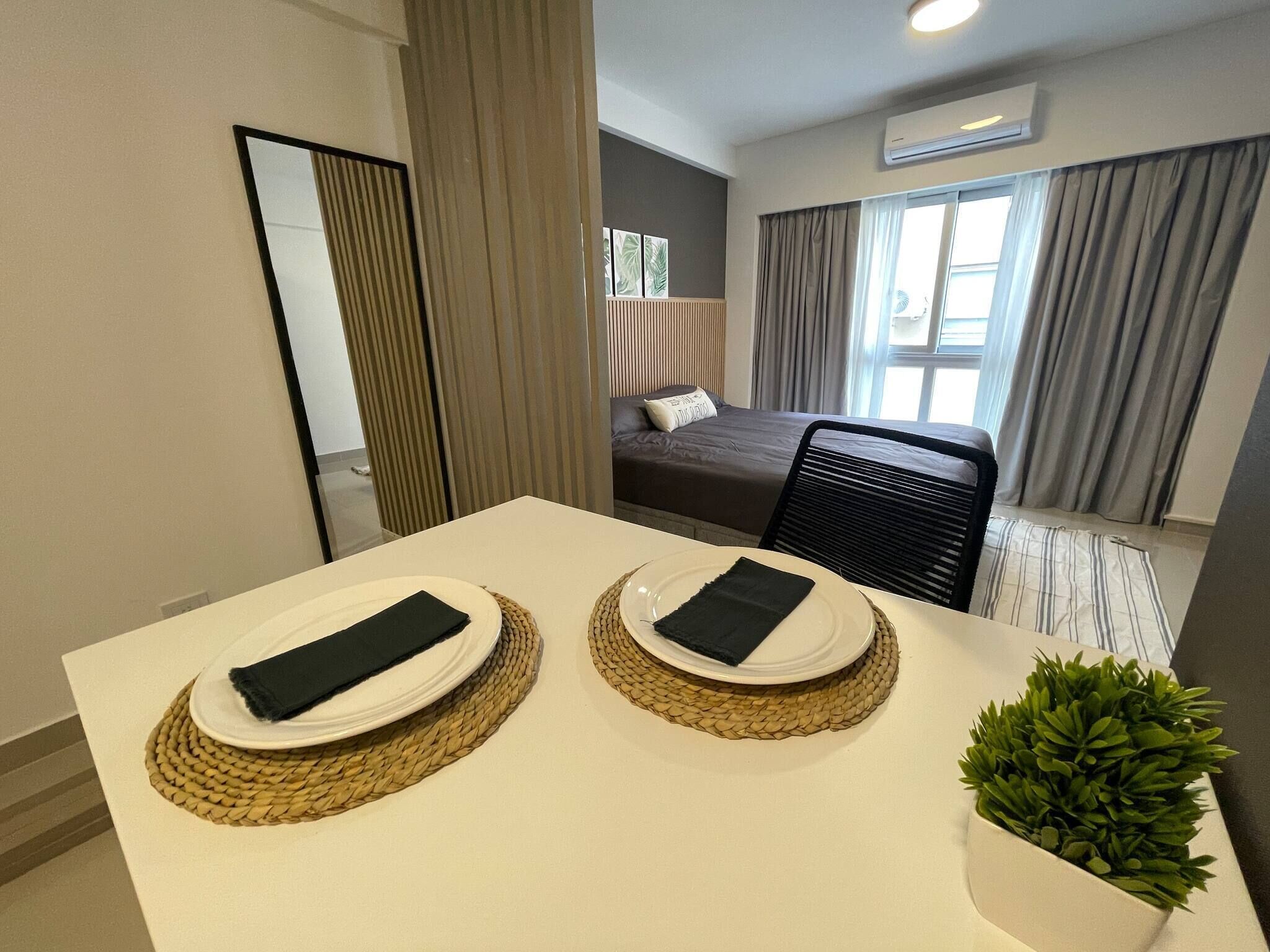A hotel room with a dining table set for two, a bed with a view, and a small potted plant.