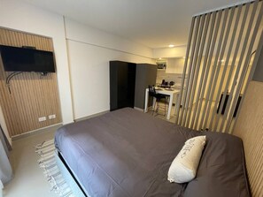 A modern hotel room with a large bed, a TV mounted on a wooden panel, a small kitchenette, and a sliding door leading to a bathroom. - Modern & Cozy Studio in San Telmo With Exclusive Service no 1 (Buenos Aires)
