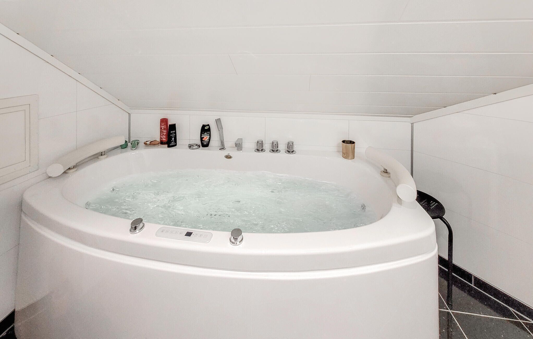 Una bañera blanca con panel de control, rodeada de artículos de aseo y un perchero para toallas.
