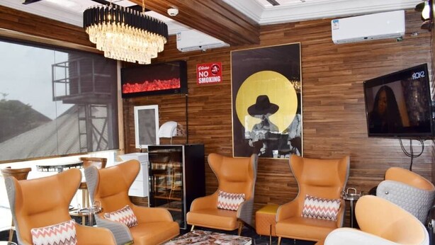 A modern interior with leather chairs, a chandelier, a large window, and a 'No Smoking' sign. - Place Tochil (Owerri)