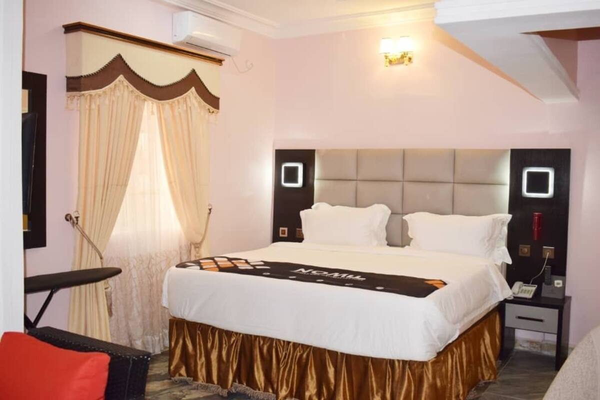 A hotel room with a large bed, a bedside table, a chair, and a window with curtains.