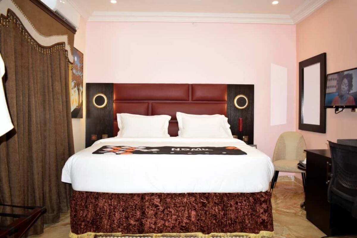 A hotel room with a large bed, two side tables, a chair, a desk, and a television.