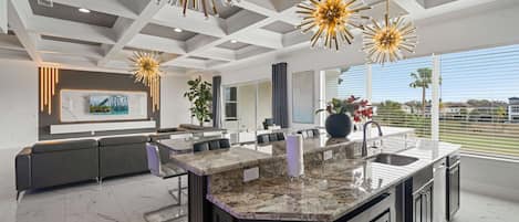 A modern kitchen with a large island, pendant lighting, and a view of the outdoors.