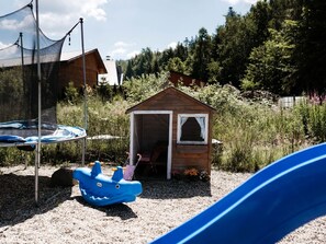 Ein Spielhaus aus Holz mit einer kleinen Veranda und einer Rutsche in der Nähe.