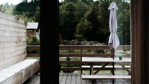 A wooden deck with a bench and picnic table, overlooking a forested area.