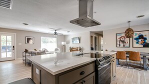 A modern kitchen with a central island, stainless steel appliances, and a dining area with two chairs. - Bab Al Shams | Pet-friendly | Great Backyard (Fredericksburg)