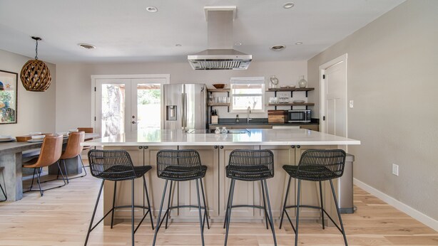A modern kitchen with a large island, bar stools, and a hanging light fixture. - Bab Al Shams | Pet-friendly | Great Backyard (Fredericksburg)