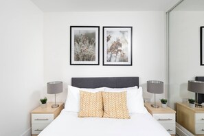 Quarto moderno com uma cama, duas mesas de cabeceira, luminárias e duas quadros na parede.