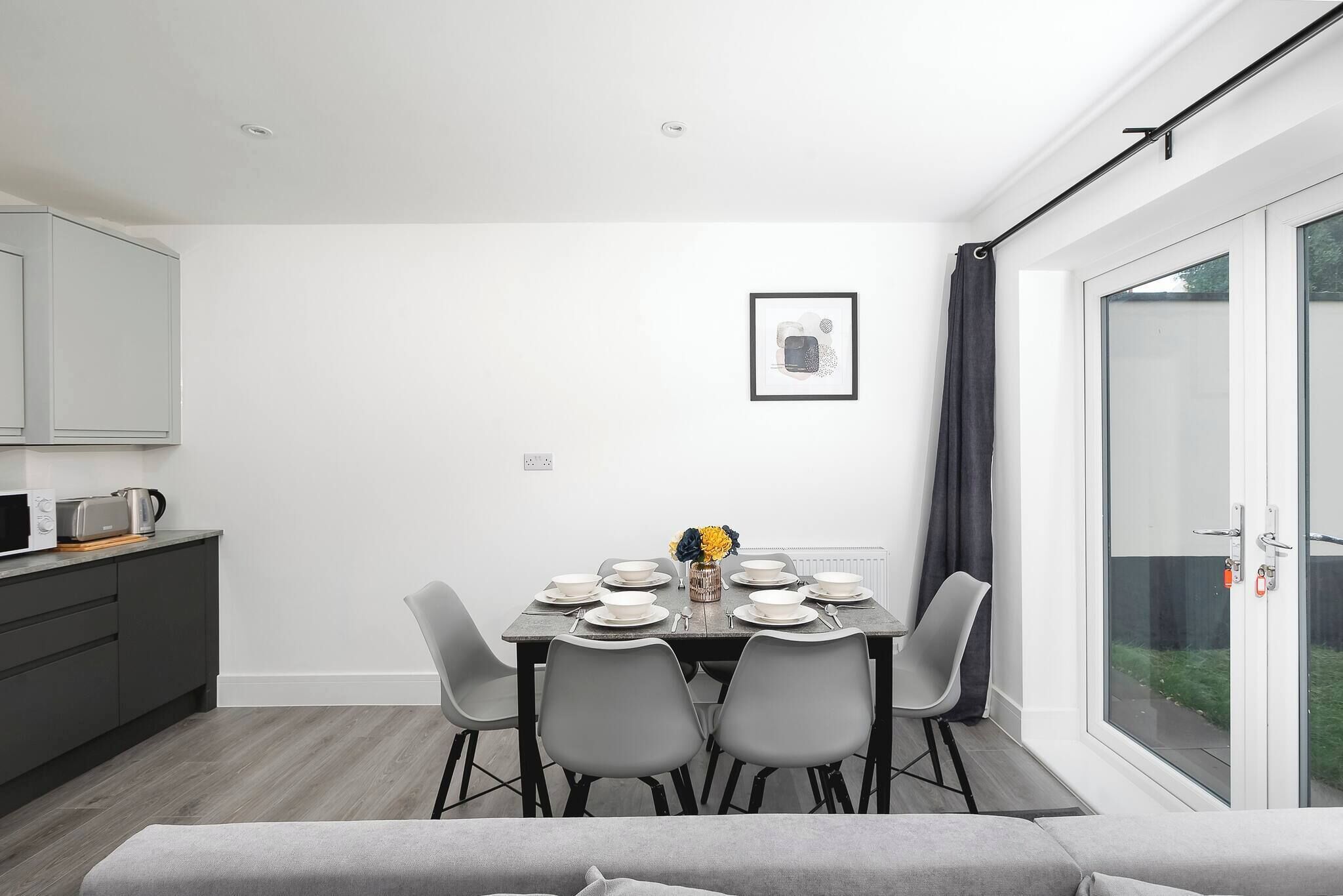 A modern dining area with a table set for four, a grey sofa, and a view through a glass door.