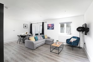 Uma sala de estar moderna com um sofá modular cinza, uma mesa de centro, uma poltrona azul e um espaço de jantar com mesa e cadeiras.